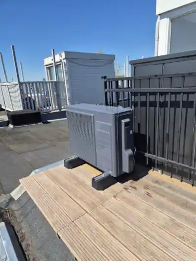Donkergrijze Intergas Xtend warmtepomp op zonnig dakterras naast hek van een Amsterdamse woning