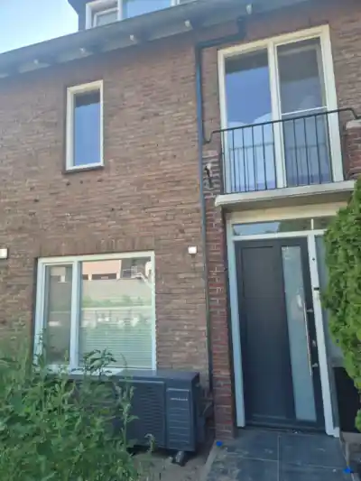 Intergas Xtend Cool Grey hybride warmtepomp in voortuin en naast deur van rijtjeshuis in Amsterdam. Koelleiding wordt langs gevel omhoog naar zolder geleid.