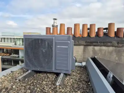 Intergas hybride warmtepomp op het dak van een Amsterdams pand met op de achtergrond oude, stenen schoorstenen