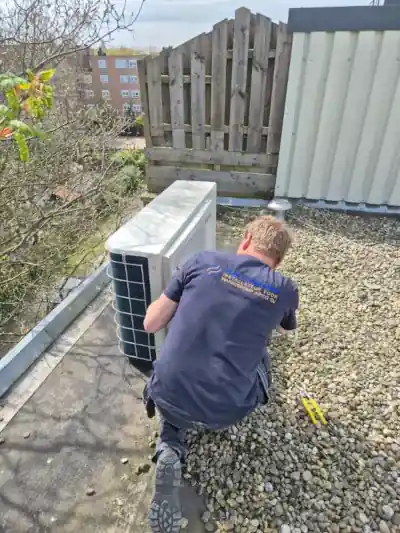 Monteur van Slim Verwarmen plaatst all electric warmtepomp op een plat Amsterdams dak