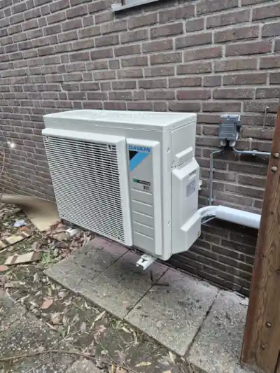 Buitenunit van een Daikin 3R split warmtepomp geplaatst op twee beugels tegen de zijmuur van een Amsterdams huis.