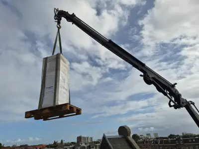 Kraan transporteert warmwatervat in doos over Amsterdamse daken